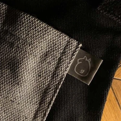 Etiqueta en tela con logo minimalista de caballo, cosida al borde de un uniforme de KOLI.